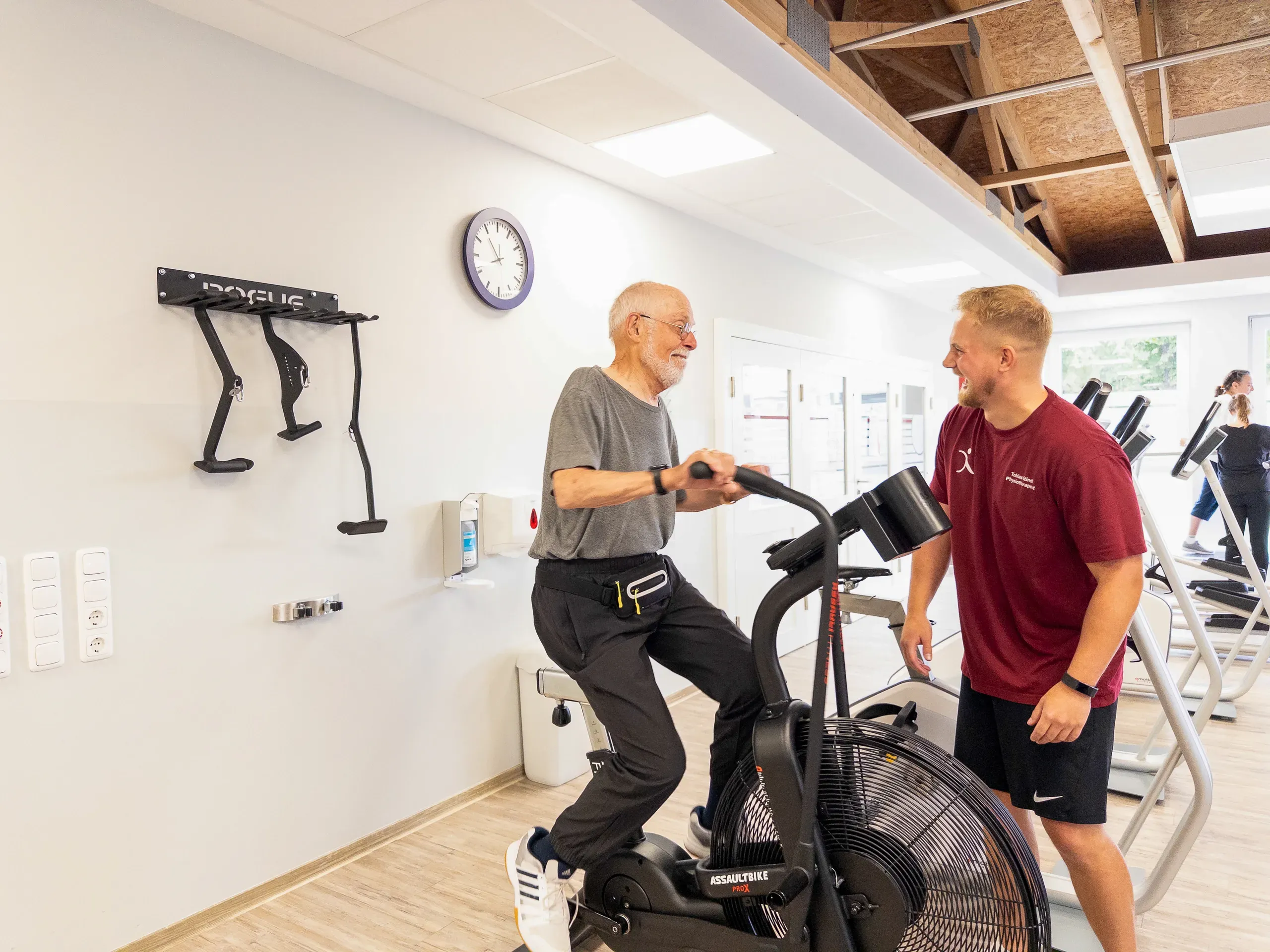 Älterer Mann auf Air-Bike im Gespräch mit Trainer