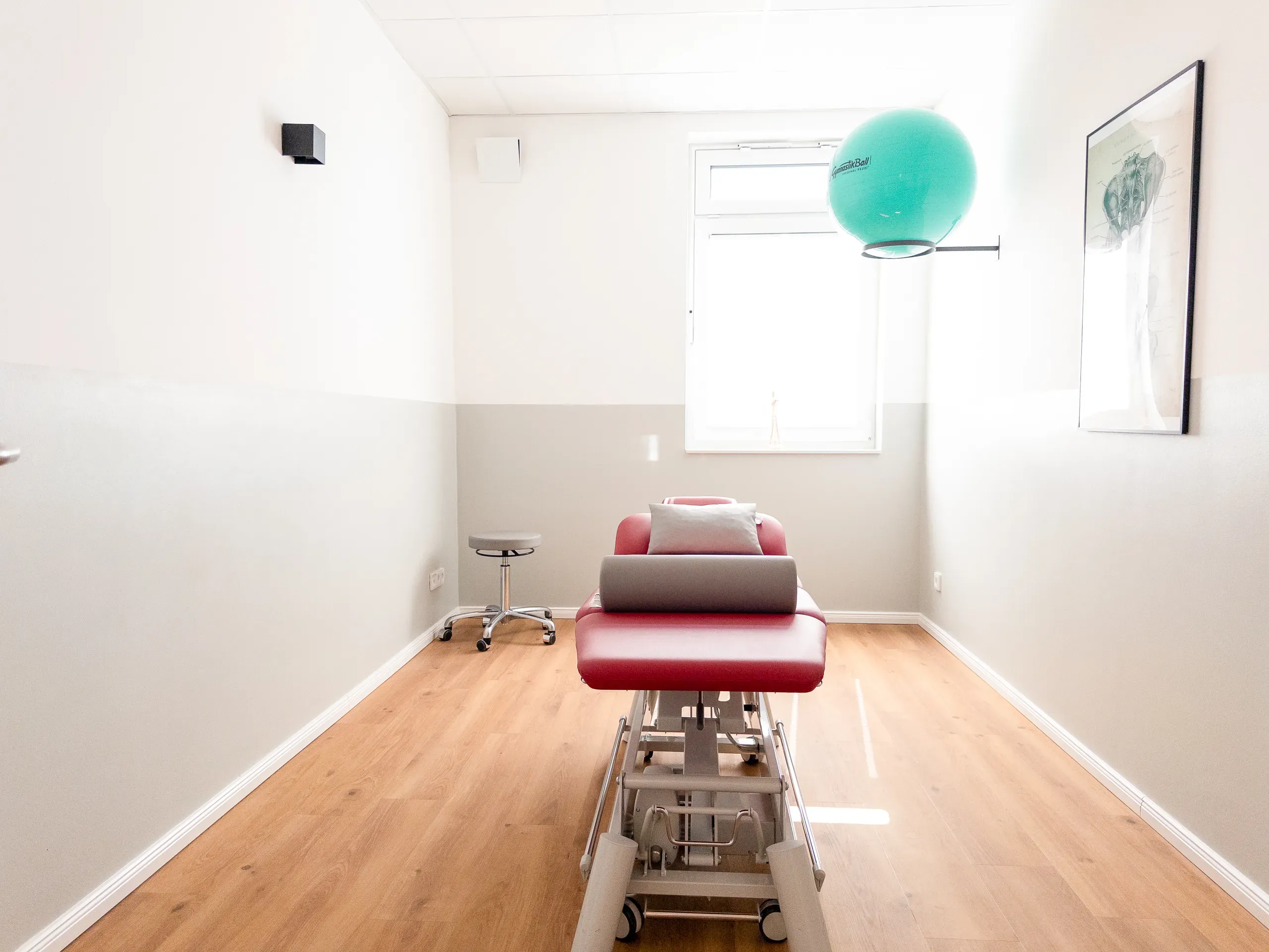 Behandlungsraum mit roter Therapieliege und Gymnastikball