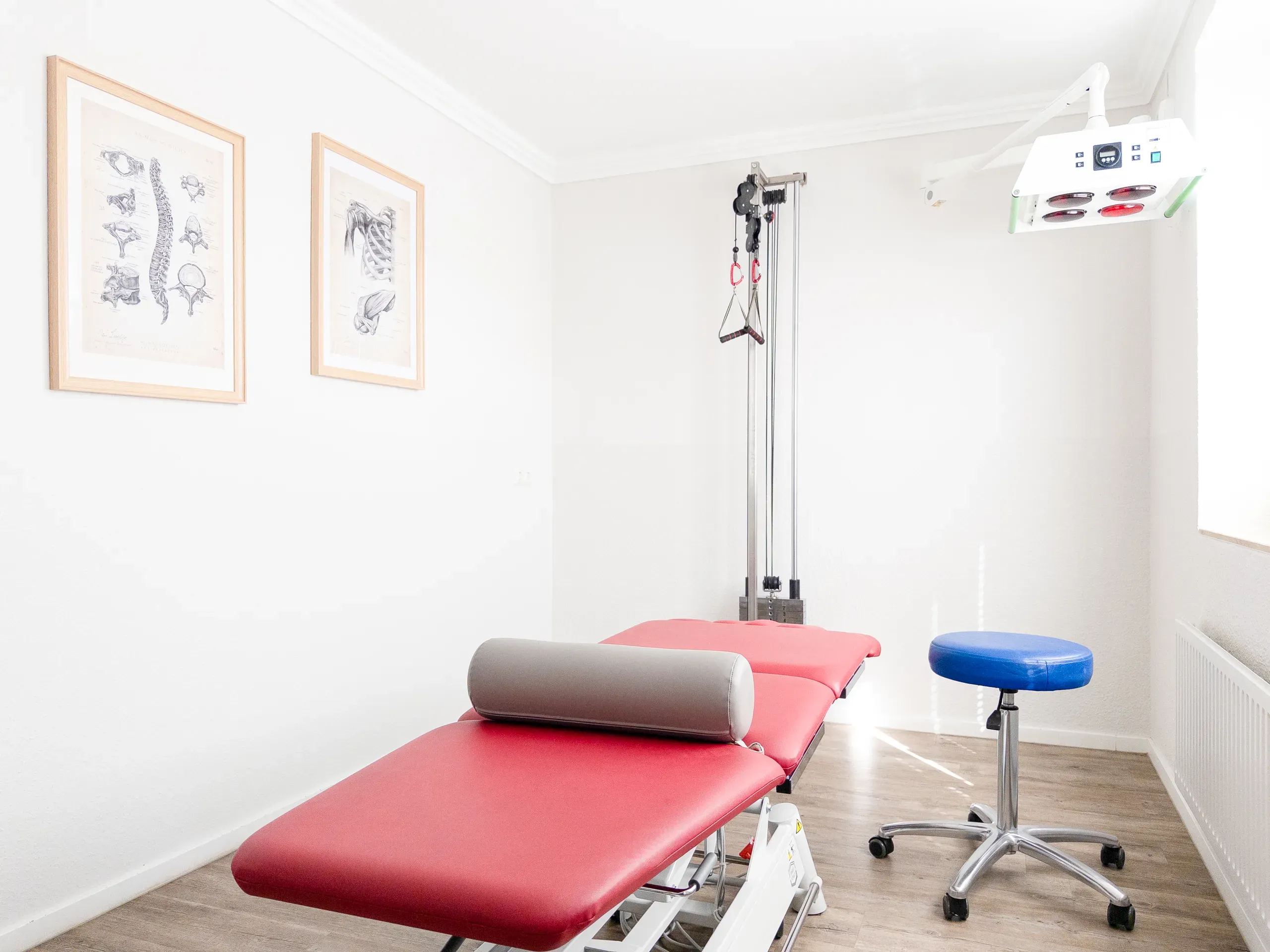 Behandlungsraum in Obenstrohe mit Therapieliege, Seilzuggerät und Anatomie-Poster
