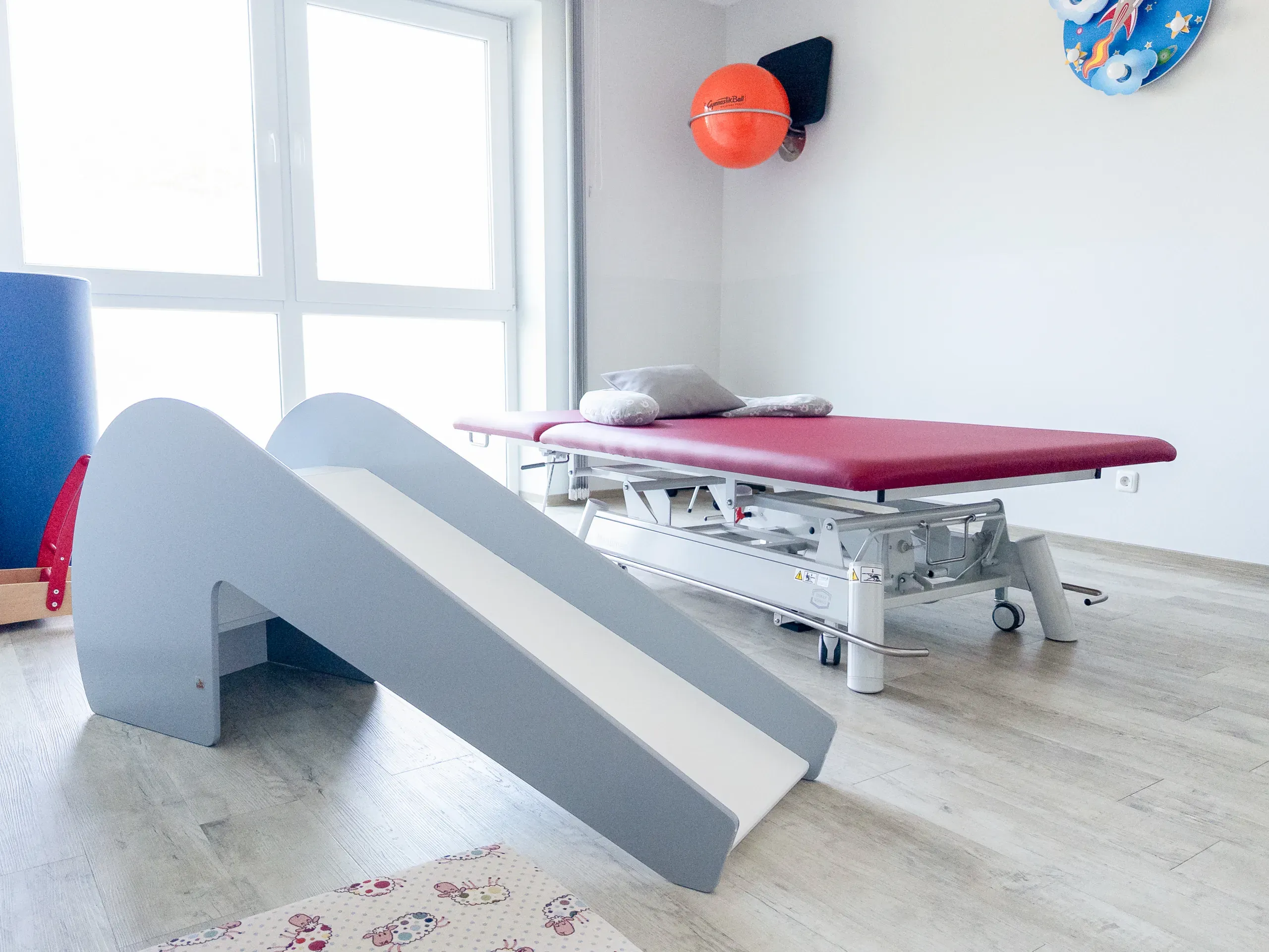 Kinder-Therapieraum mit Holzrutsche und roter Behandlungsliege
