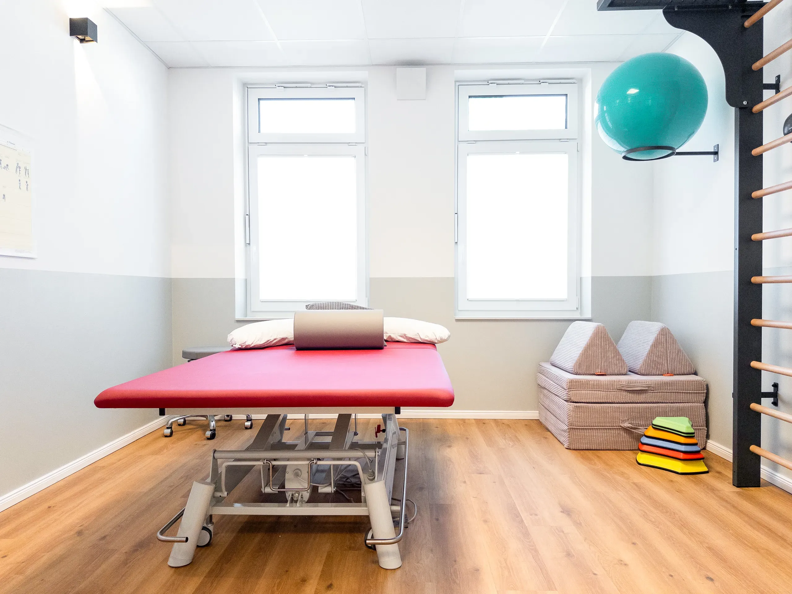 Behandlungsraum in Rastede mit roter Behandlungsliege, Sprossenwand und Gymnastikball